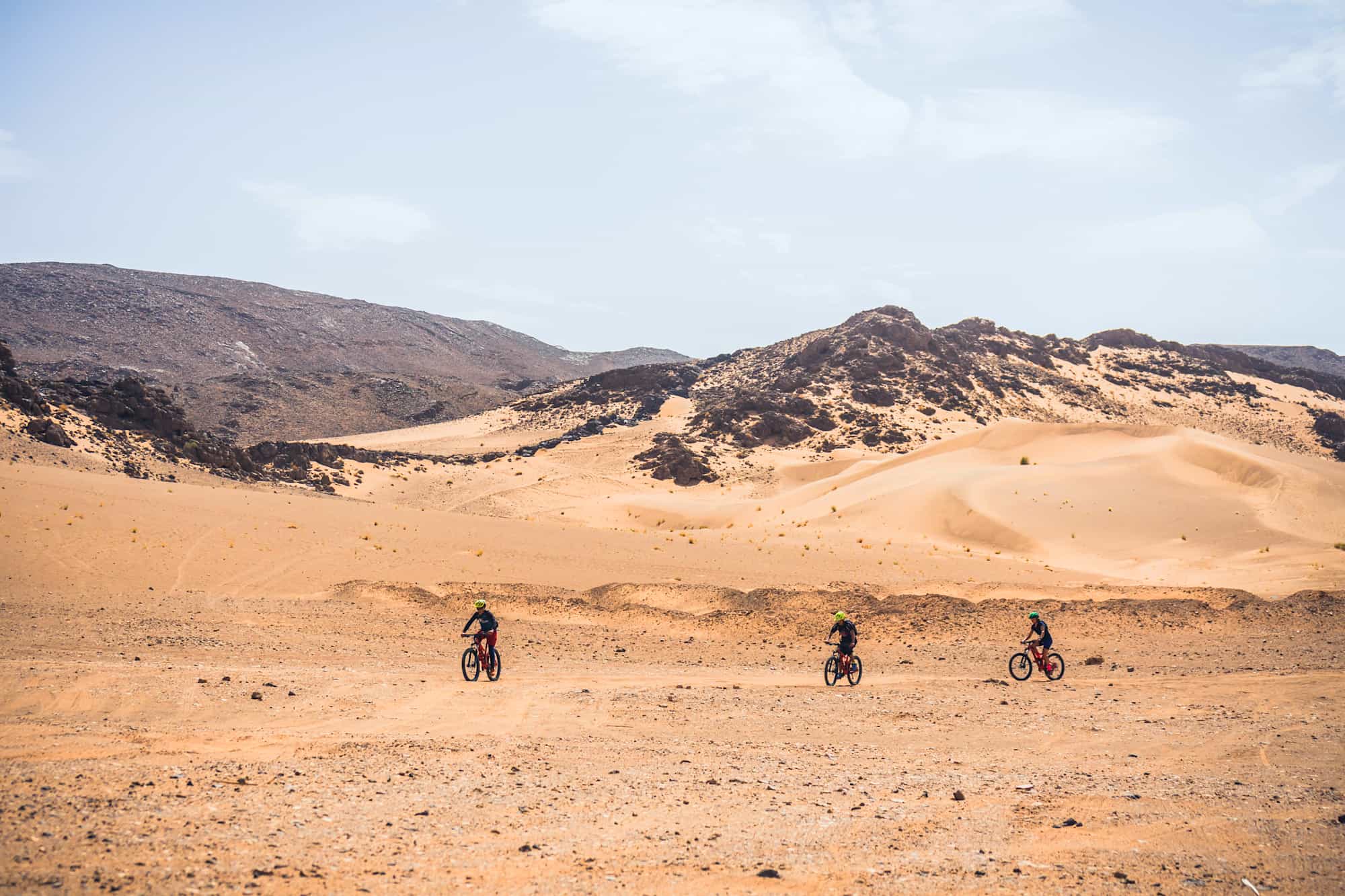 Three cyclists riding in the Sahara desert, Morocco