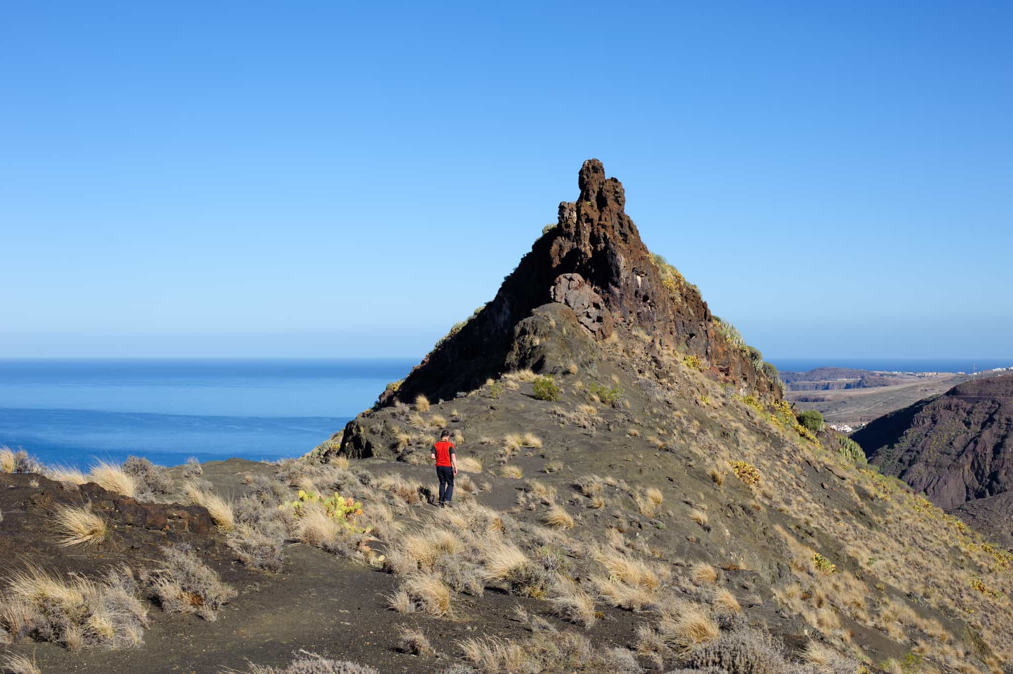 Hikers on arid, volcanic terrain in Gran Canaria, with the ocean in the background.