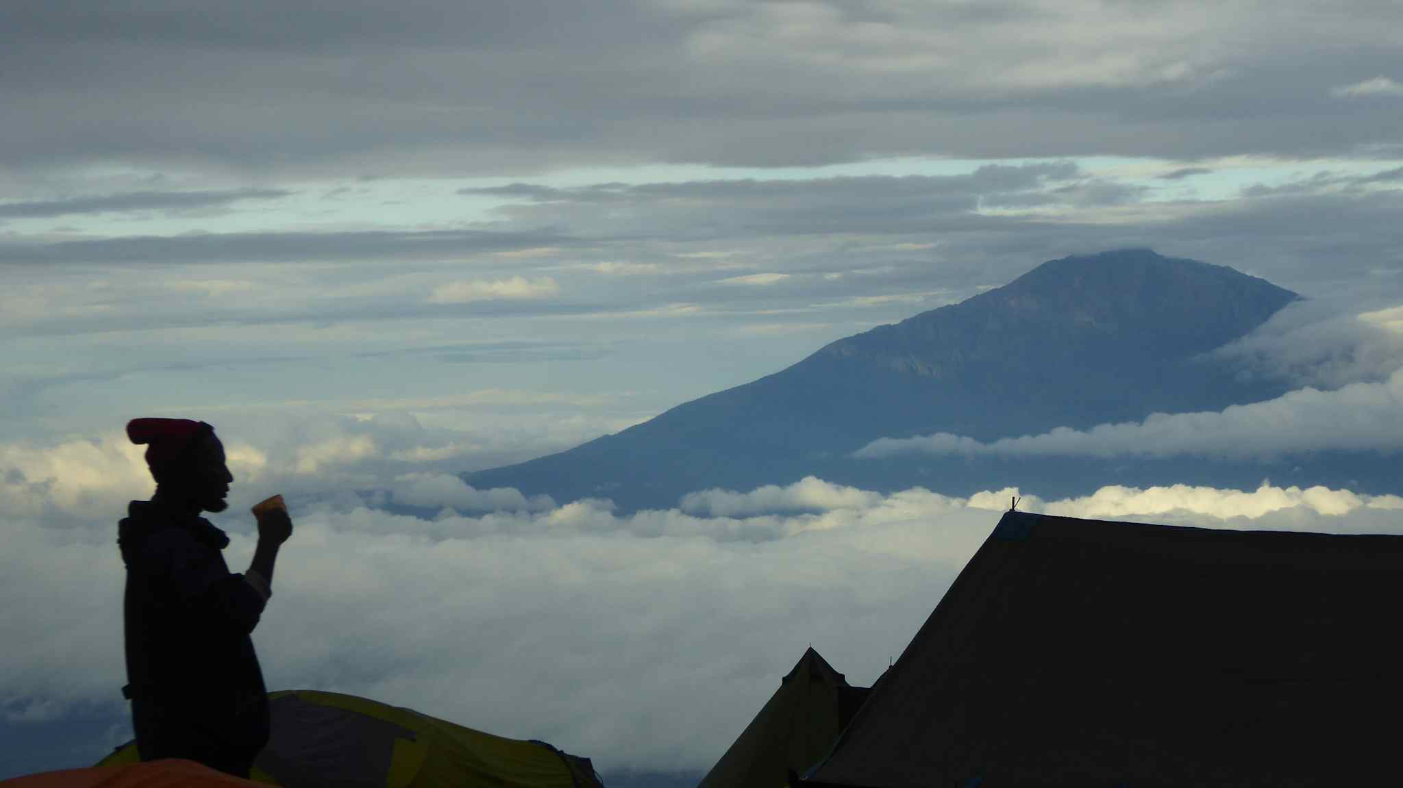Views from camp on the Shira Plateau, Kilimanjaro, with a man drinking tea silhouetted against the mountains.