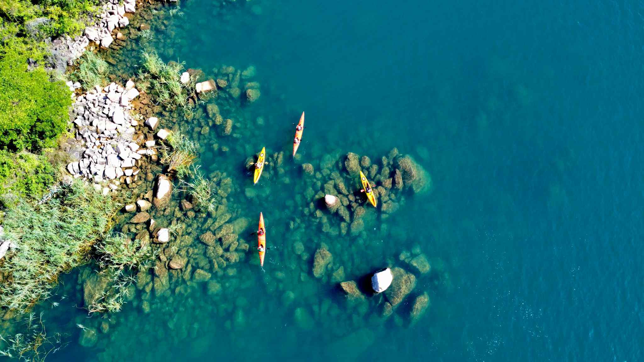 Kayakers on Tanzania's Lake Tanganiyka with rocky shoreline from above. Photo: Host Lake Shore Lodge
