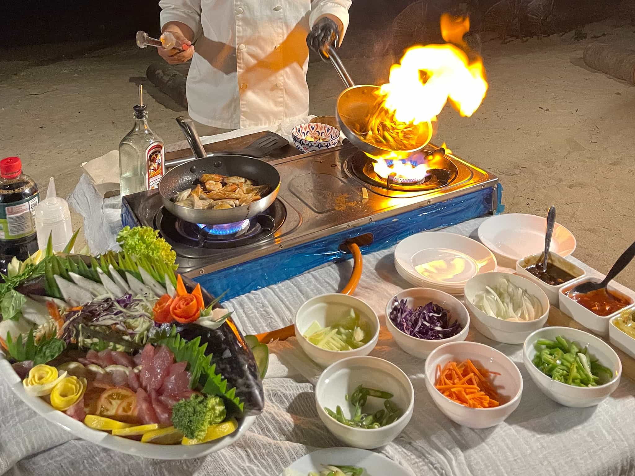 Food served on a long table under a thatched roof on the beach. Photo: Host/Agasas