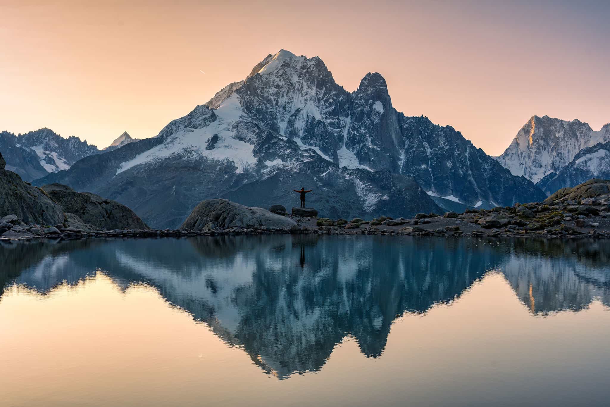 Hiker stands behind alpine lake with mountain view in the background