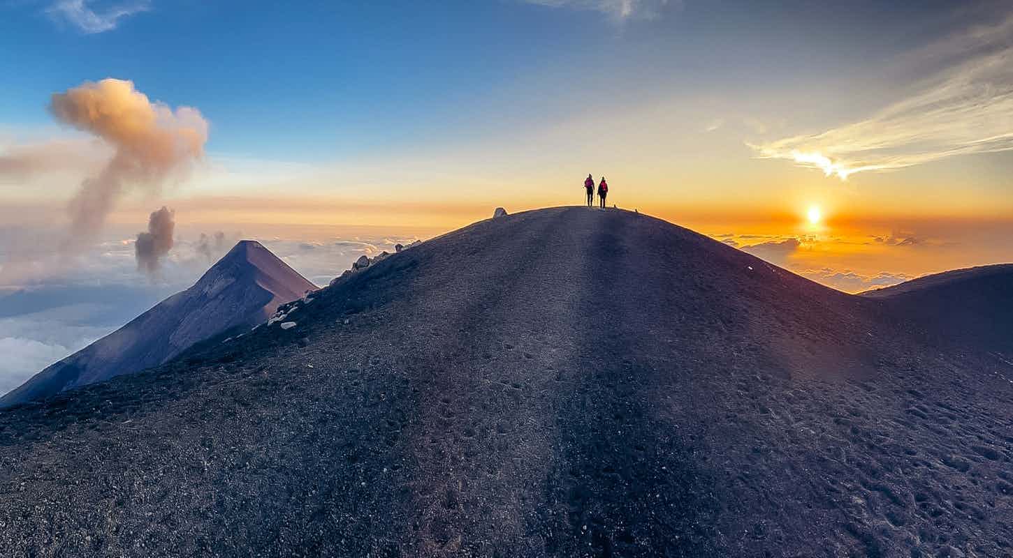 Two hikers walking on Acatenango volcano summit at sunset, Guatemala. 