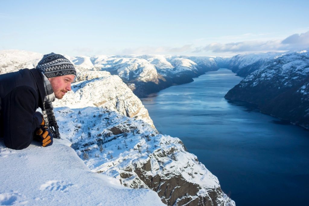 A man laying down near the edge of a fjord, a wise stance in order to stay safe.