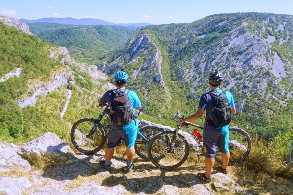 Two cyclists look down on the stunning forests and canyons of Slovenia.