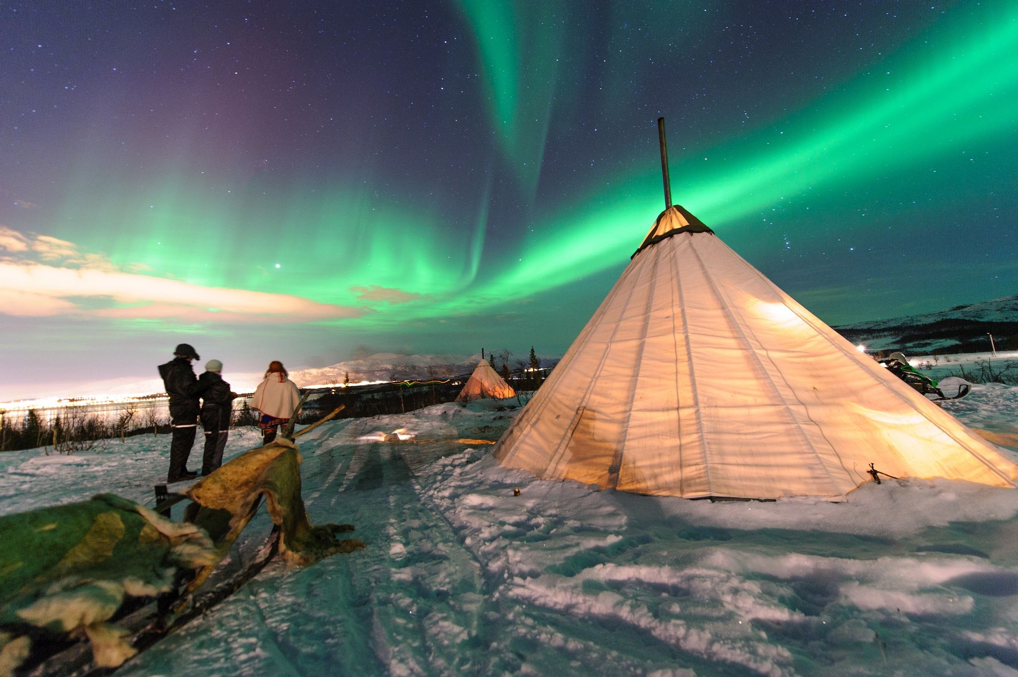 A bell tent beneath the aurora borealis, with snow and forest all around.