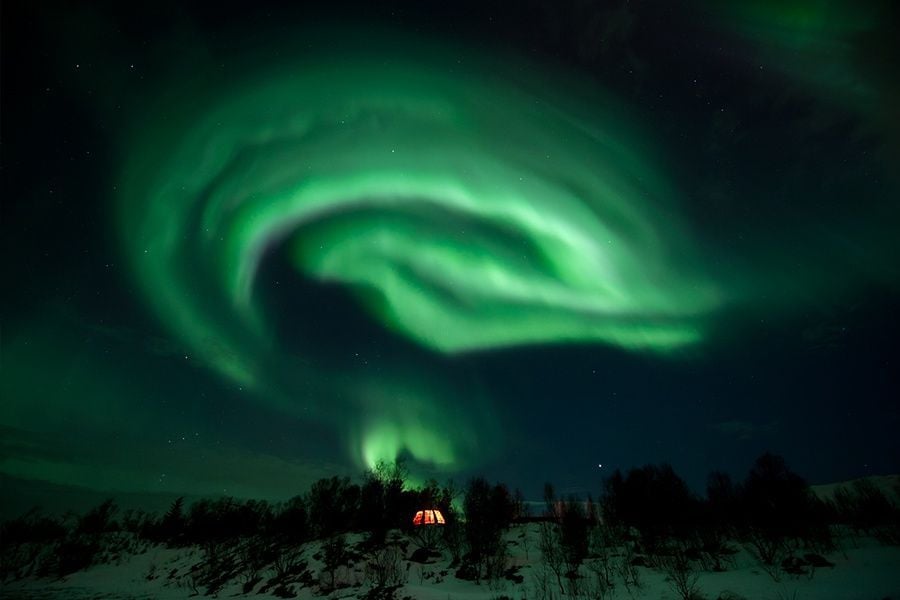 The northern lights circle in the sky above a tent.