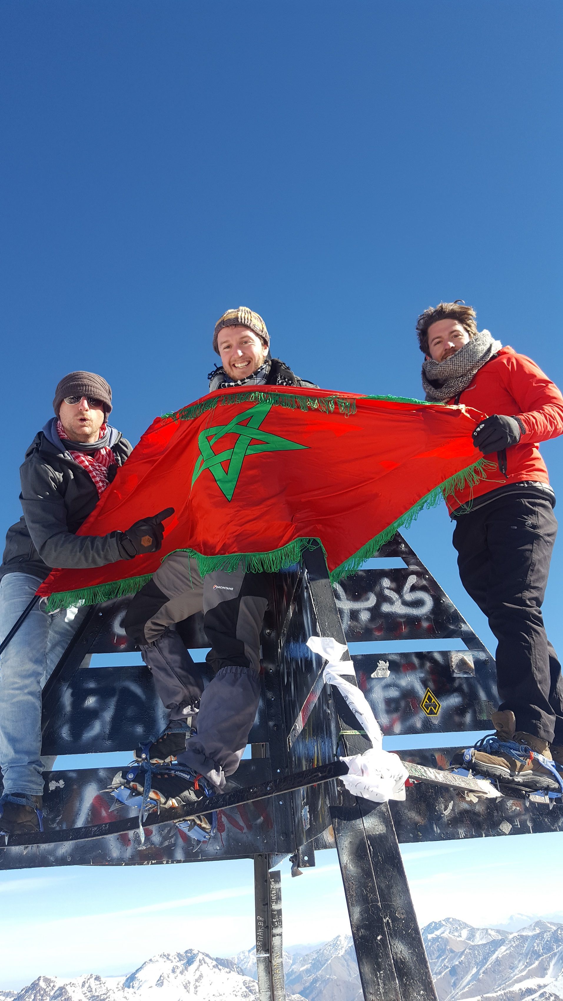 Atlas Mountains, Morocco Three climbers hold a Morocco flag up on the summit of Mount Toubkal.