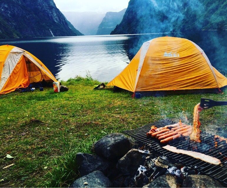 A campsite on the Naeroyfjord in Norway, with someone grilling sausages in the foreground