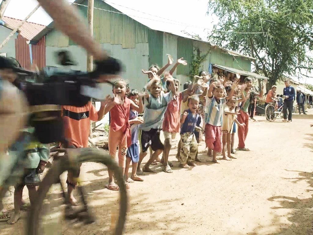 Social Cycles, cycling past a bunch of children in Cambodia.