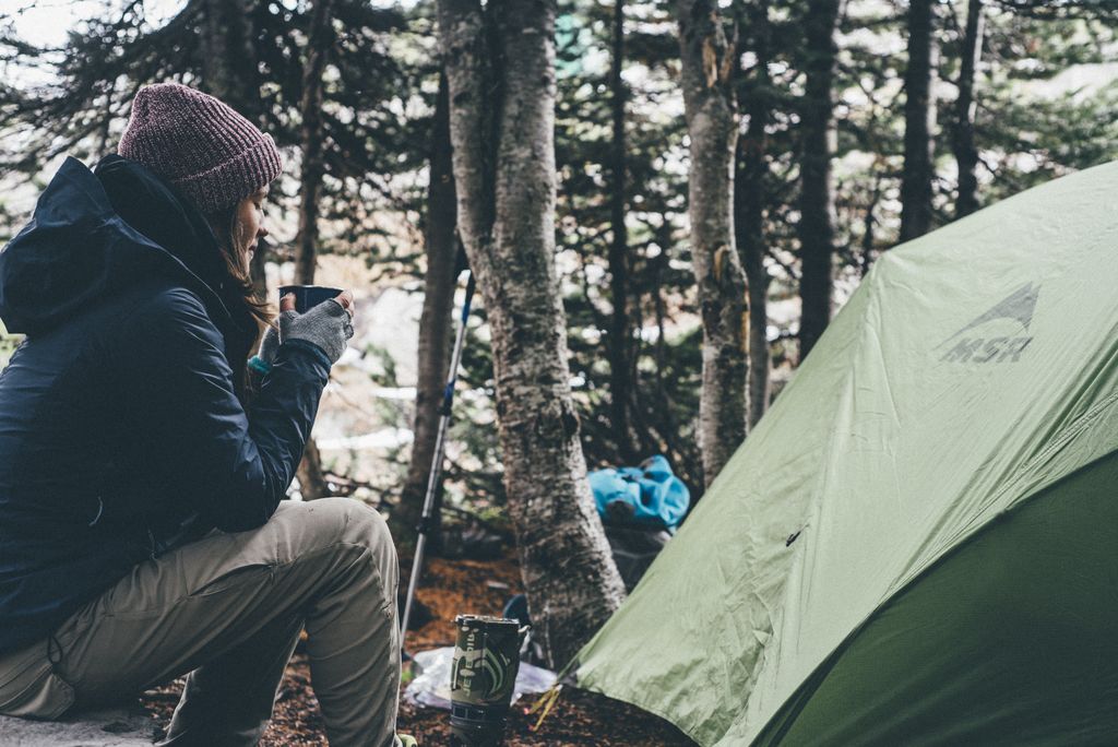 A woman drinks a mug of tea near a tent at a wild campsite in Norway.