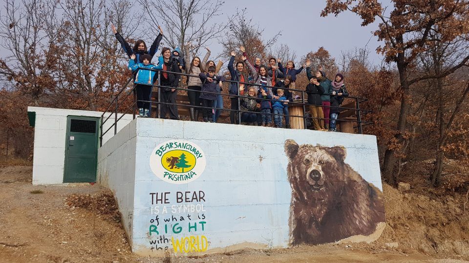 Children and their parents posing outdoors, standing on a platform at the Bear Sanctuary of Prishtina.