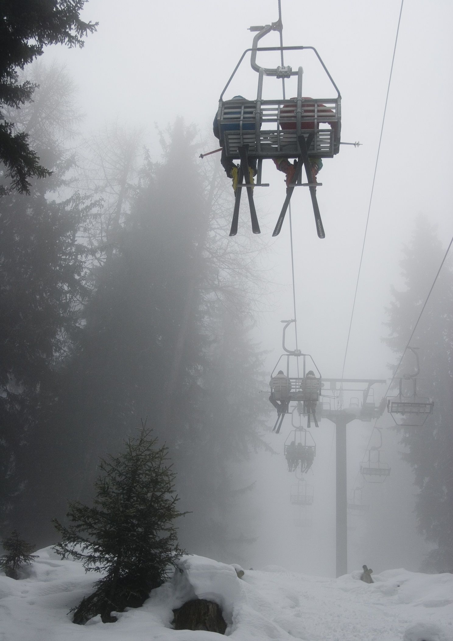 Skiers on a ski lift on a misty day.