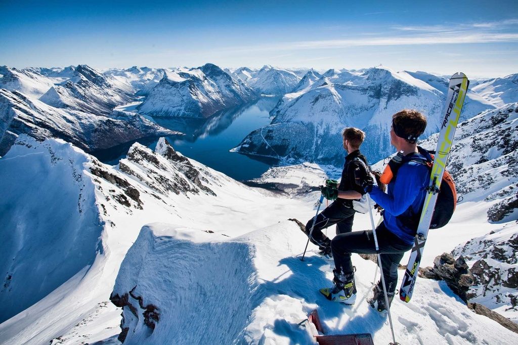 Two men with skis strapped to their backs looked out over snowy mountains.
