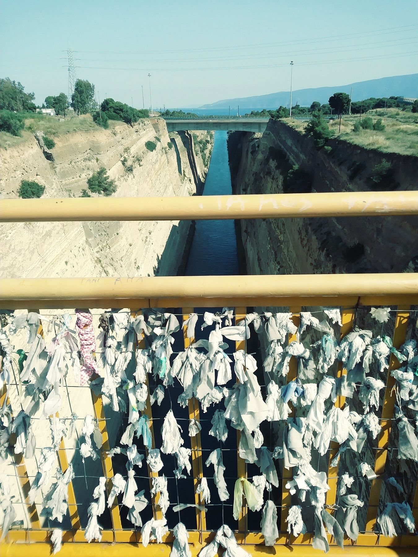 The Corinth Canal, a bridge with ribbons tied to it in the foreground.