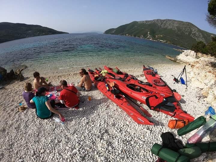 Campers sharing a meal on a beach of Thillia Island, Greece, with kayaks pulled ashore.