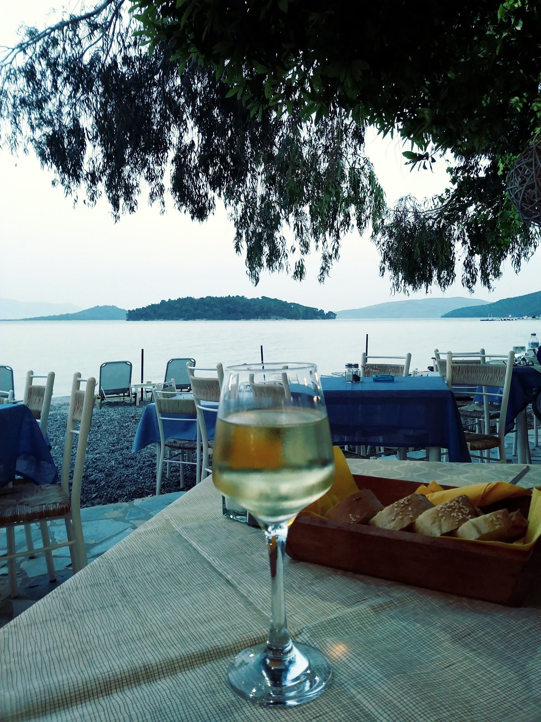 A glass of chilled white wine and some bread on a restaurant table in Greece.