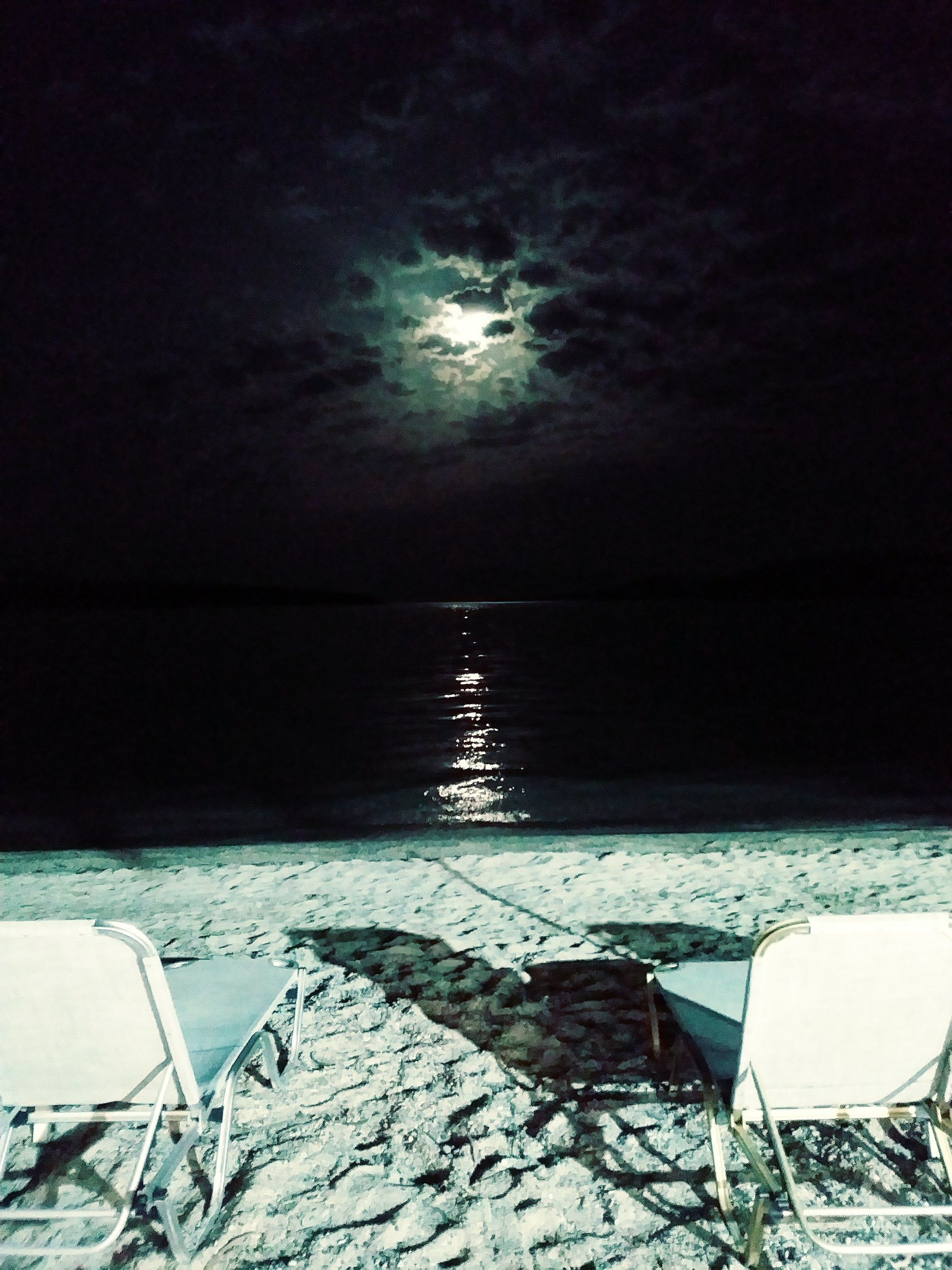 Two deckchairs on a beach under the full moon, in Greece.