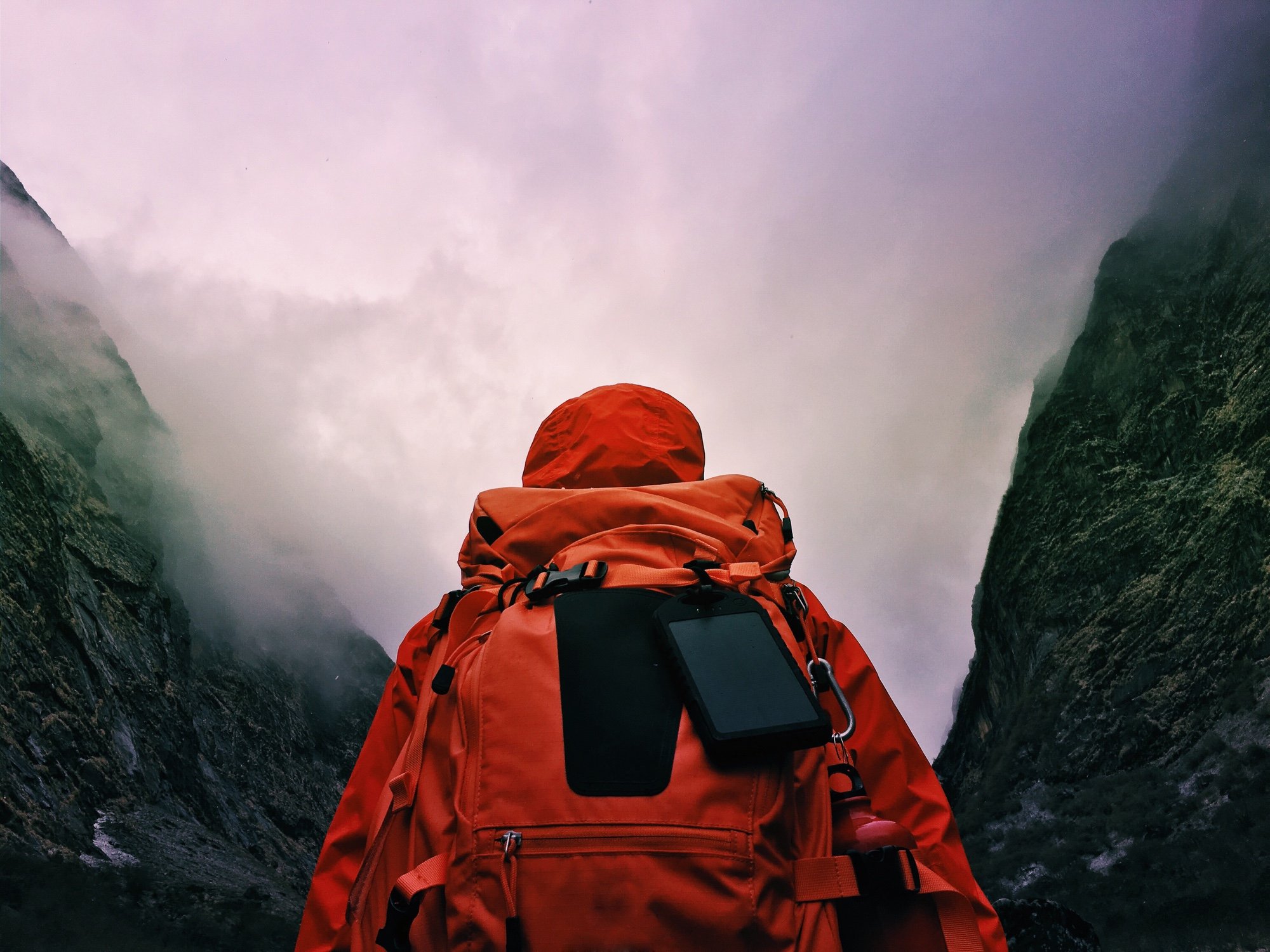 A cyclist in full waterproof gear looks up at sheer, mist-shrouded mountains