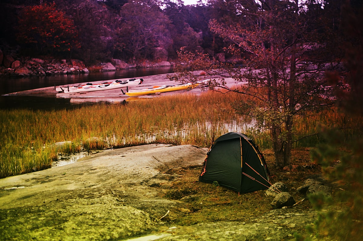 A tent on the rocky shore of an island of the Saint Anna Archipelago; kayaks pulled ashore in the background.