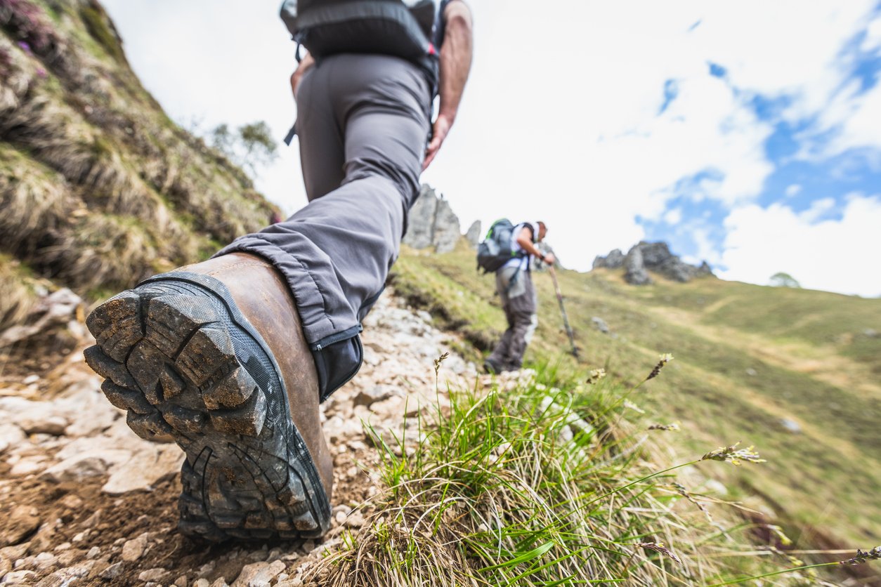 The soul of a hiking boot raises up from the floor. Two hikers are making their way up an unknown mountain.