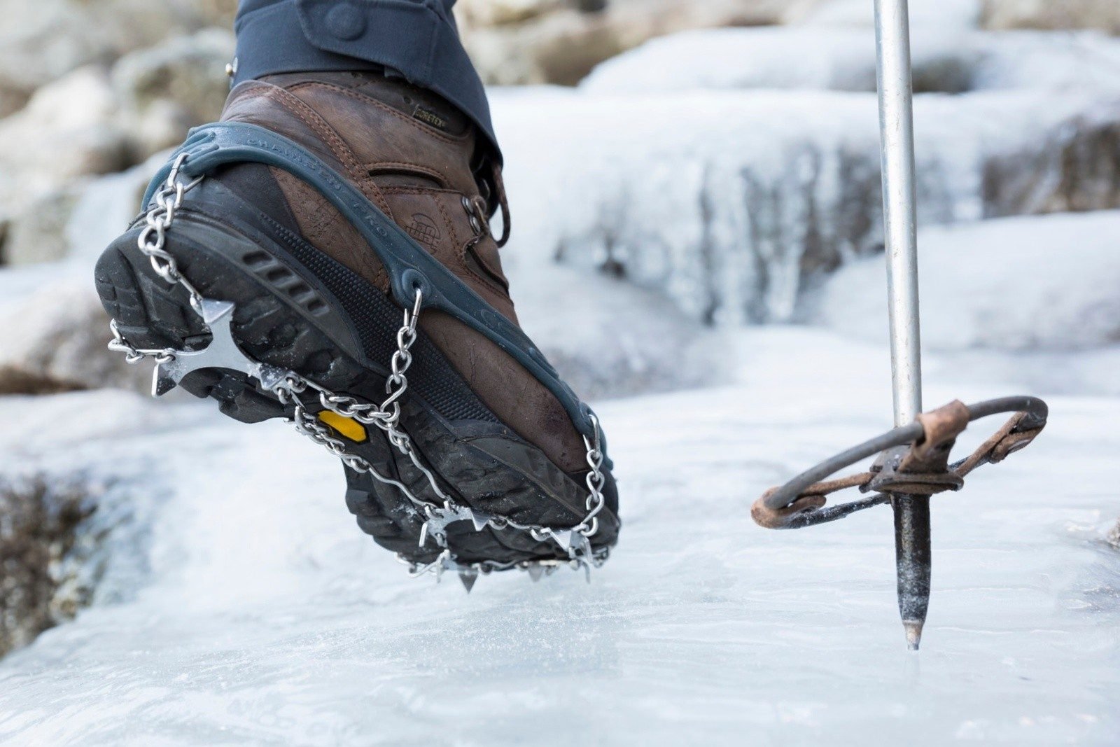 A close up of a hiking boot with crampons on it, and the tip of a hiking pole.