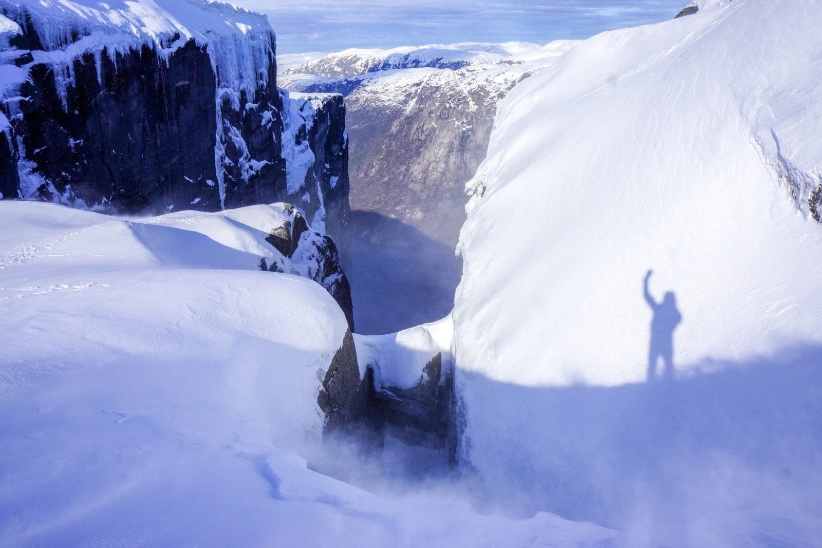 The Kjerag Boulder, Norway, covered in snow - you can see the shadow of a hiker taking a selfie.