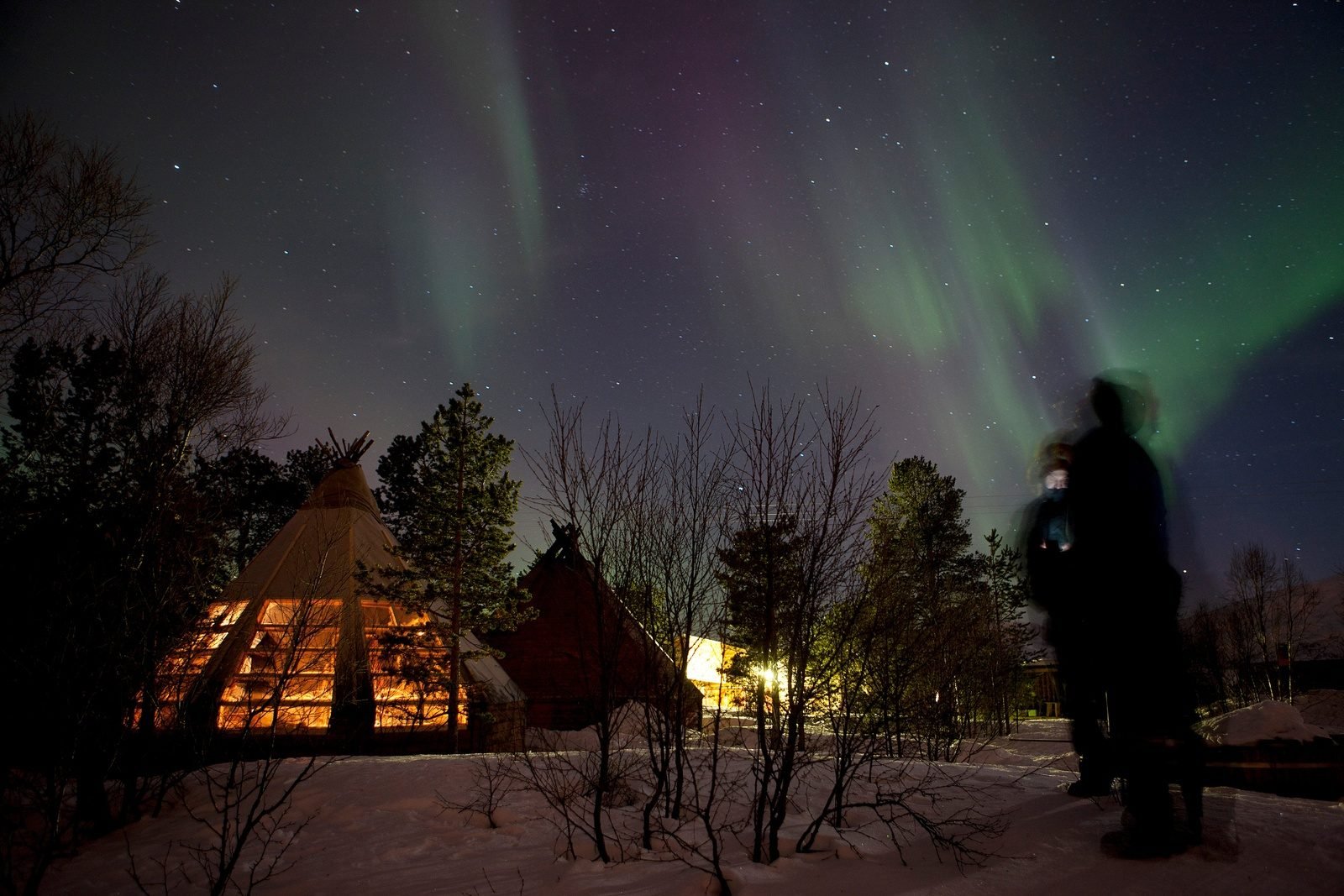 People looking at the northern lights outside their teepee camp.