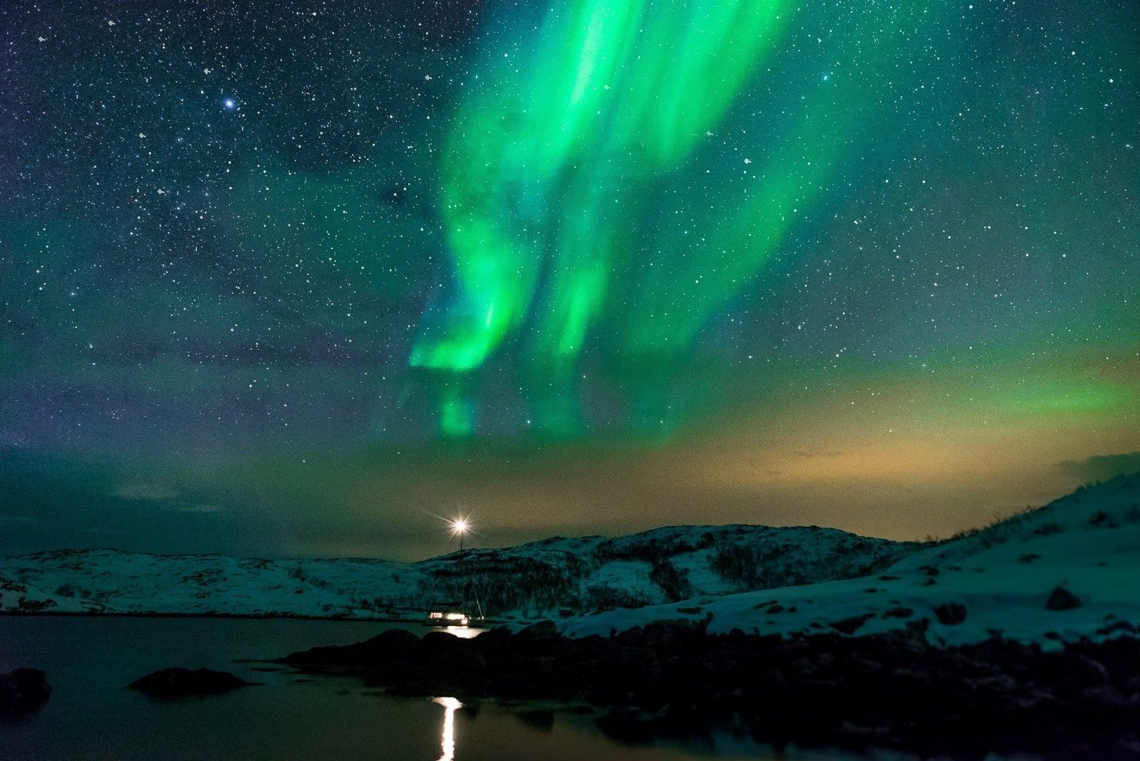 Northern Lights shining above a snowy fjord.