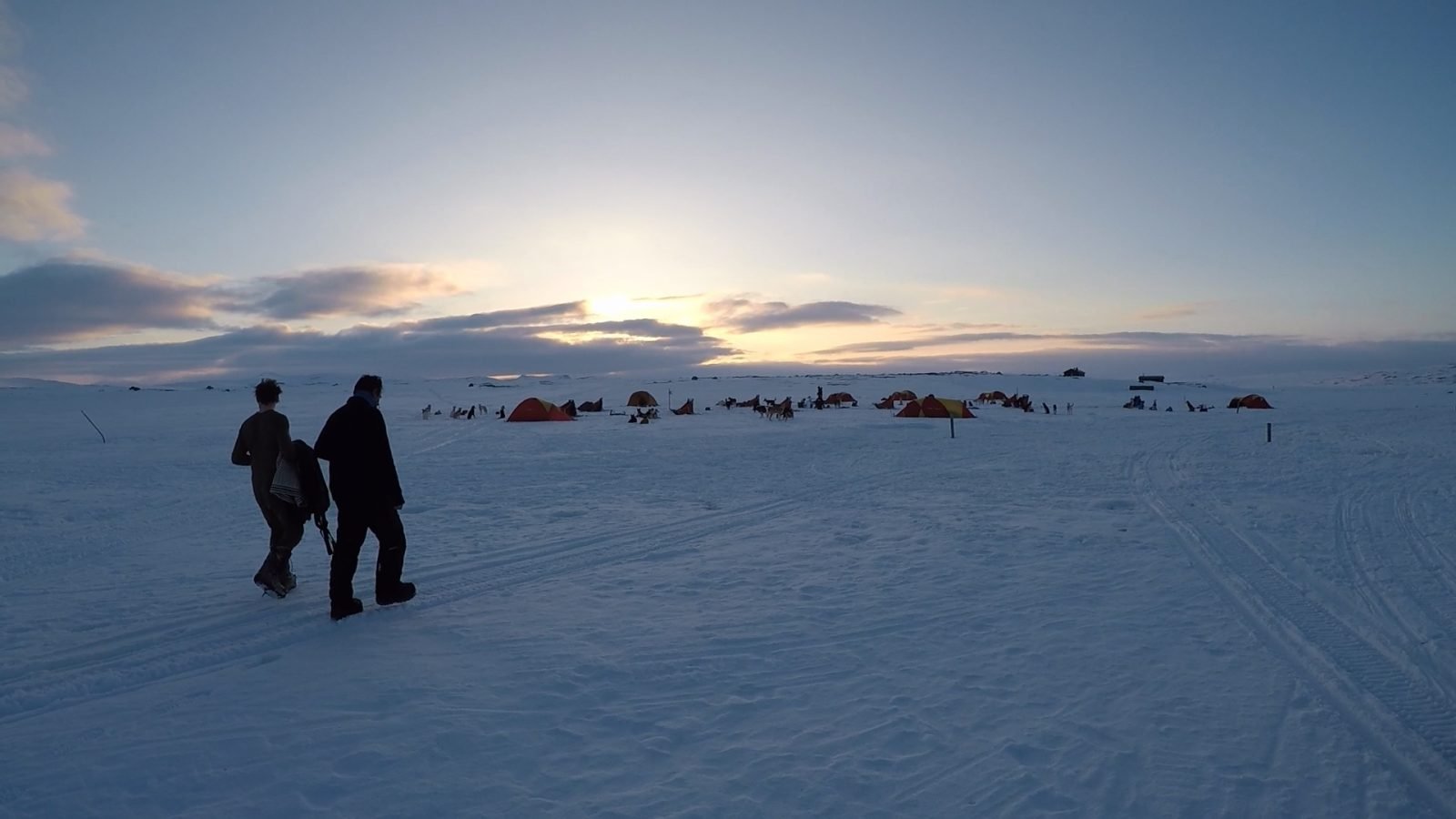 A campsite surrounded by snow, under the midnight sun.