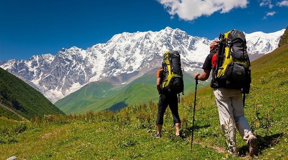 Two hikers trekking in the Republic of Georgia, snowcapped mountains in the background.