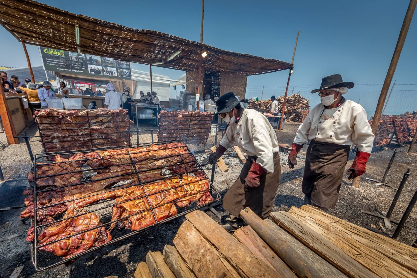 Men grilling pork over a fire pit at the Mistura Food Festival in Lima, Peru.