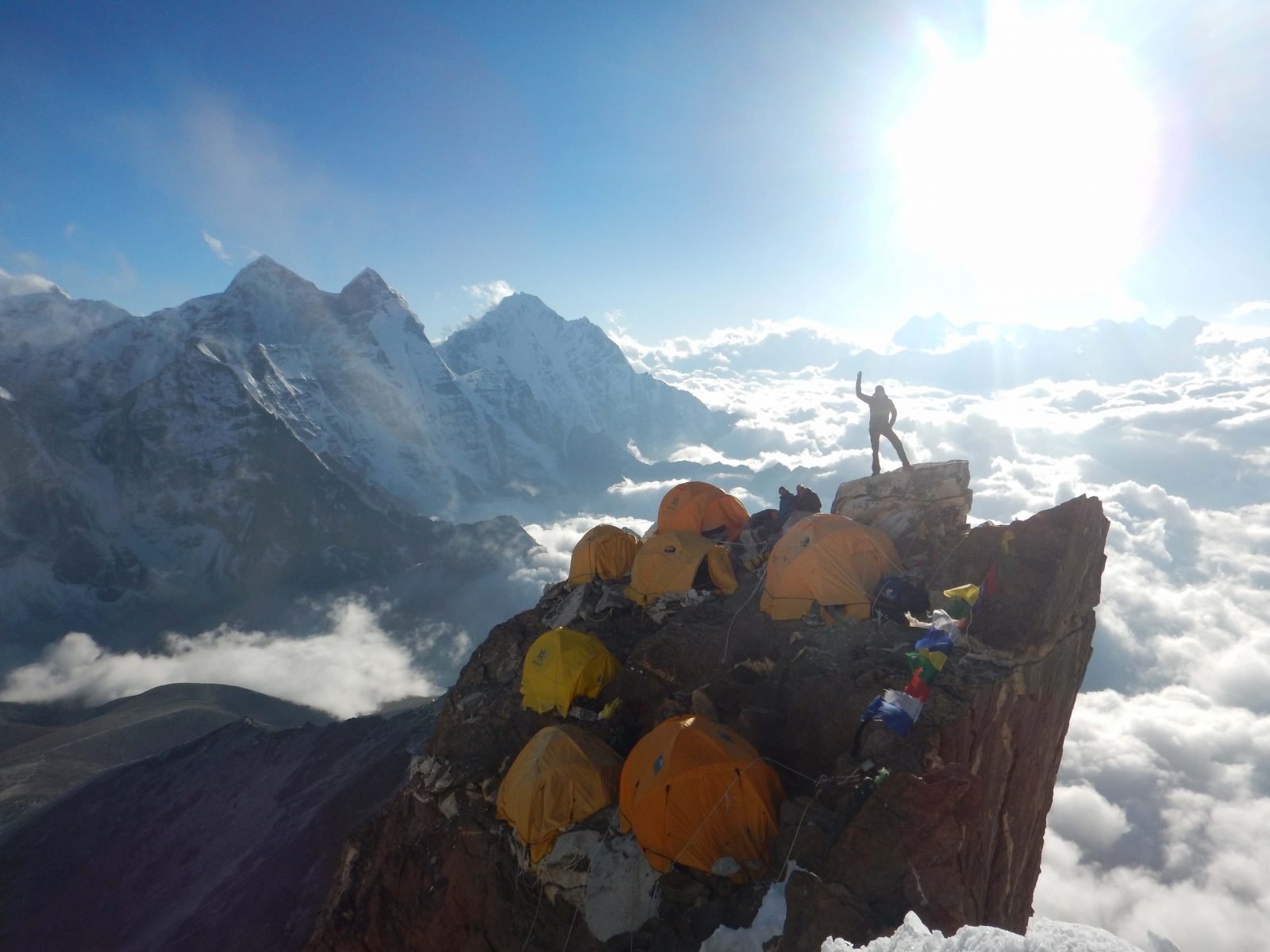 A man poses at the top of Ama Dablam camp, perched precariously on a Himalayan crag and surrounded by a sea of clouds.