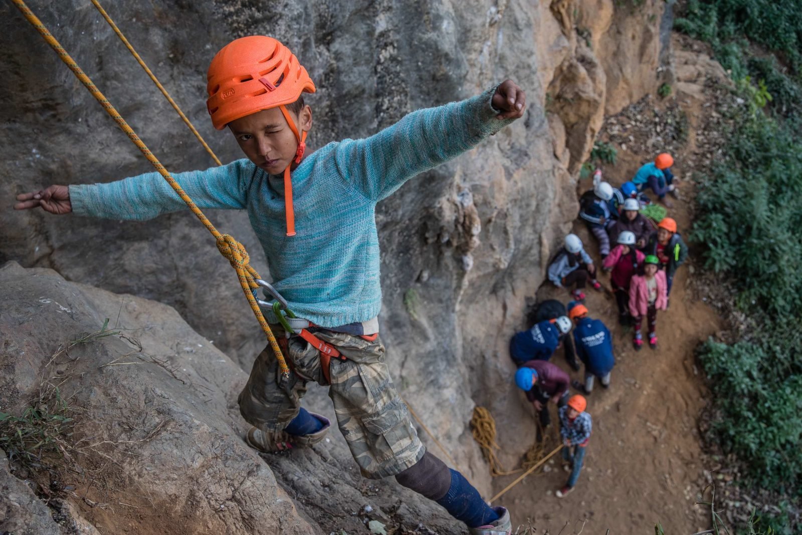 A young boy poses on a rock face while climbing in Nepal.