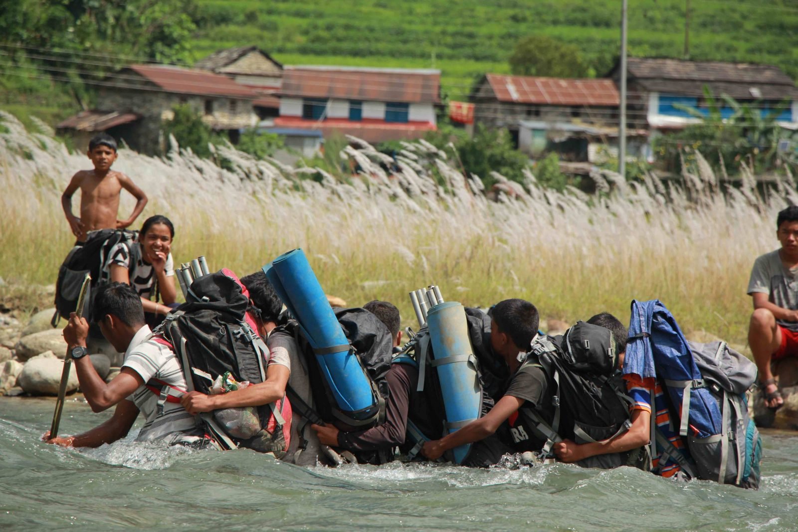 A youth hiking group waist-deep in water as they cross a river.