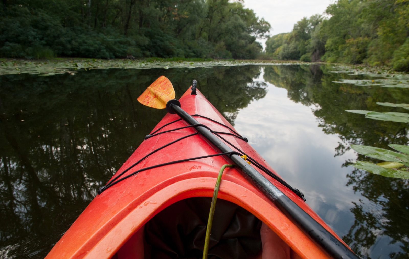 A kayak in a river, with the paddle strapped to the top.