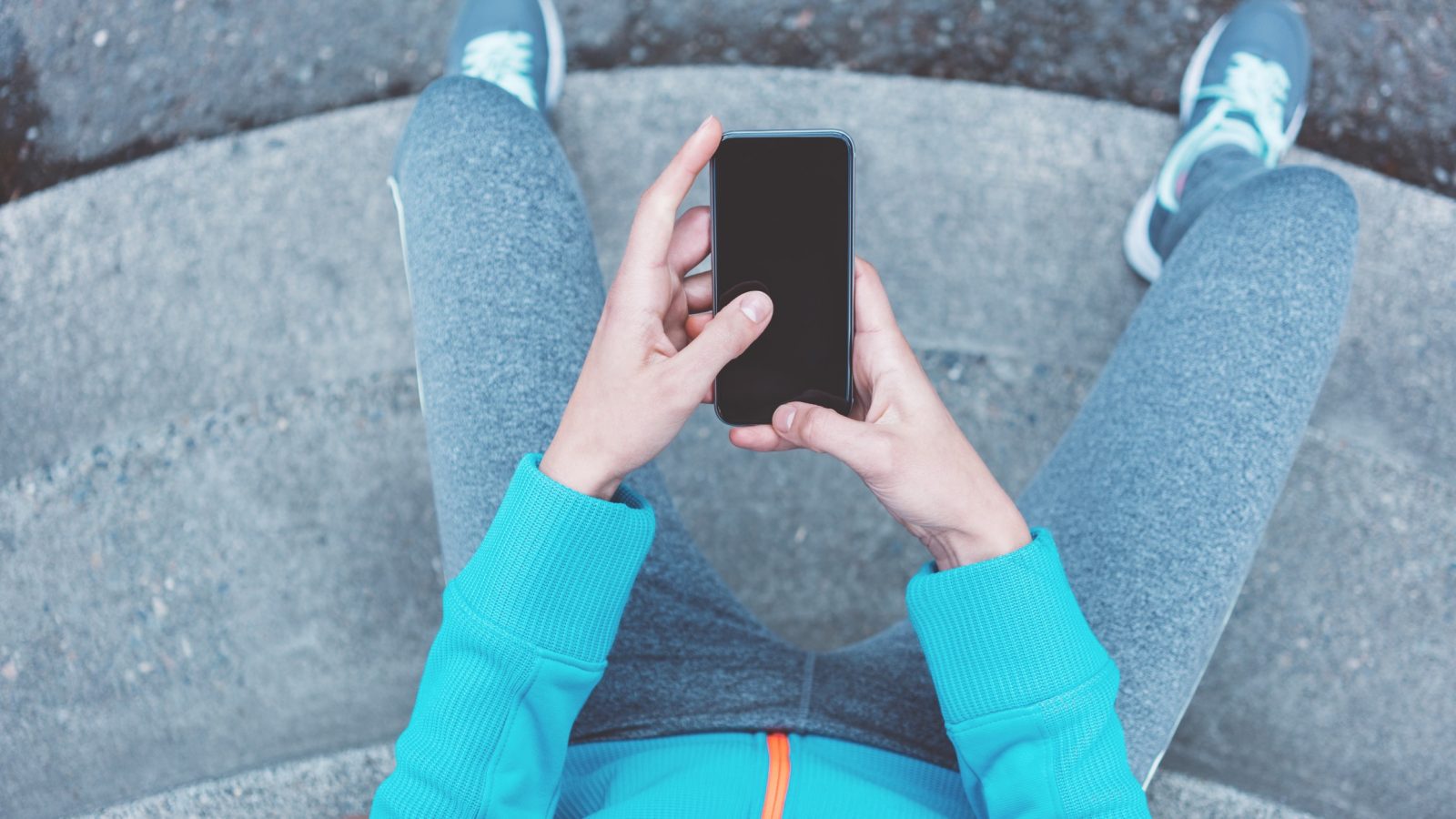 A close up of someone in running gear, sitting down holding a phone in their hands