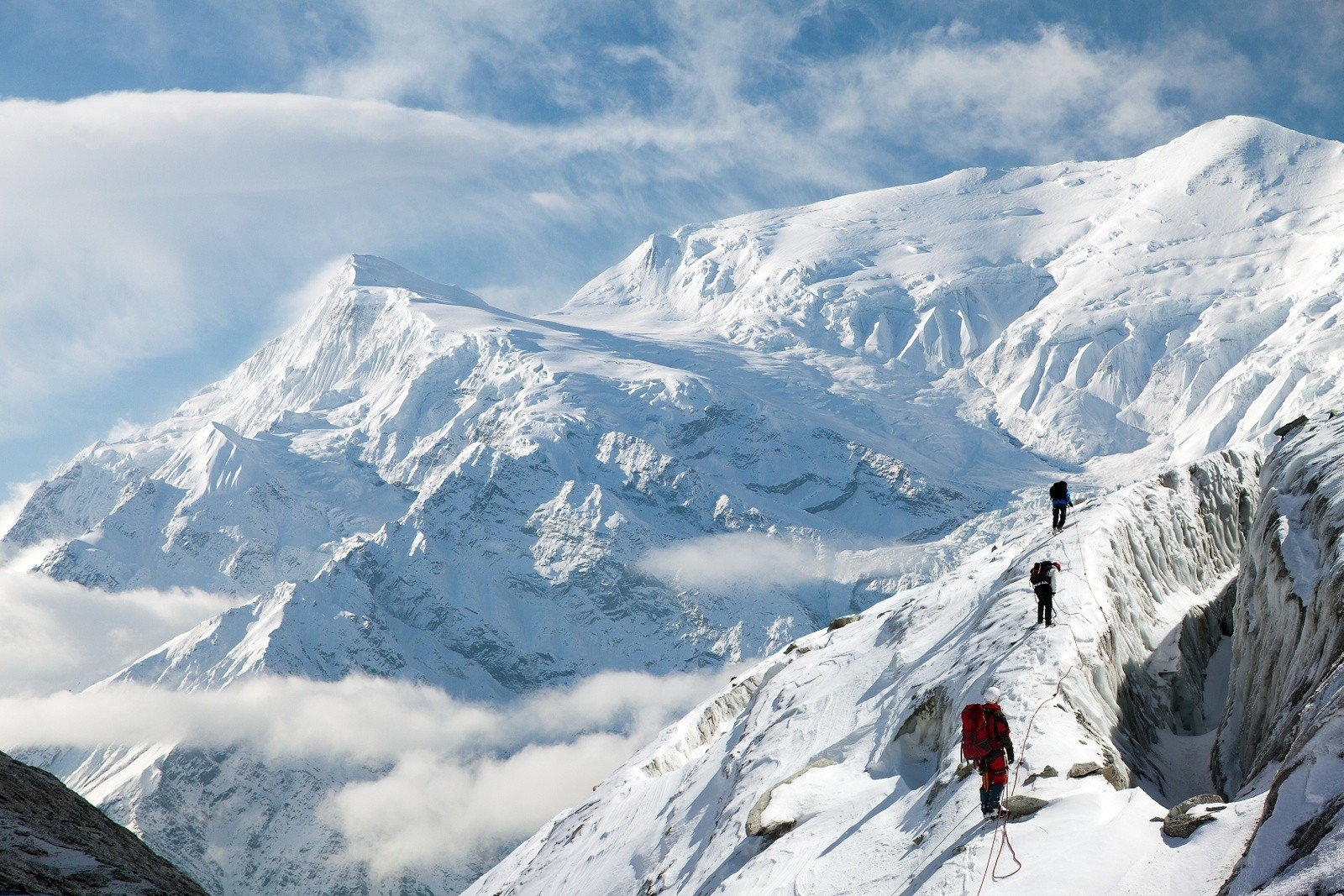 Mountaineers make their way along the top of a snowy mountain pass.