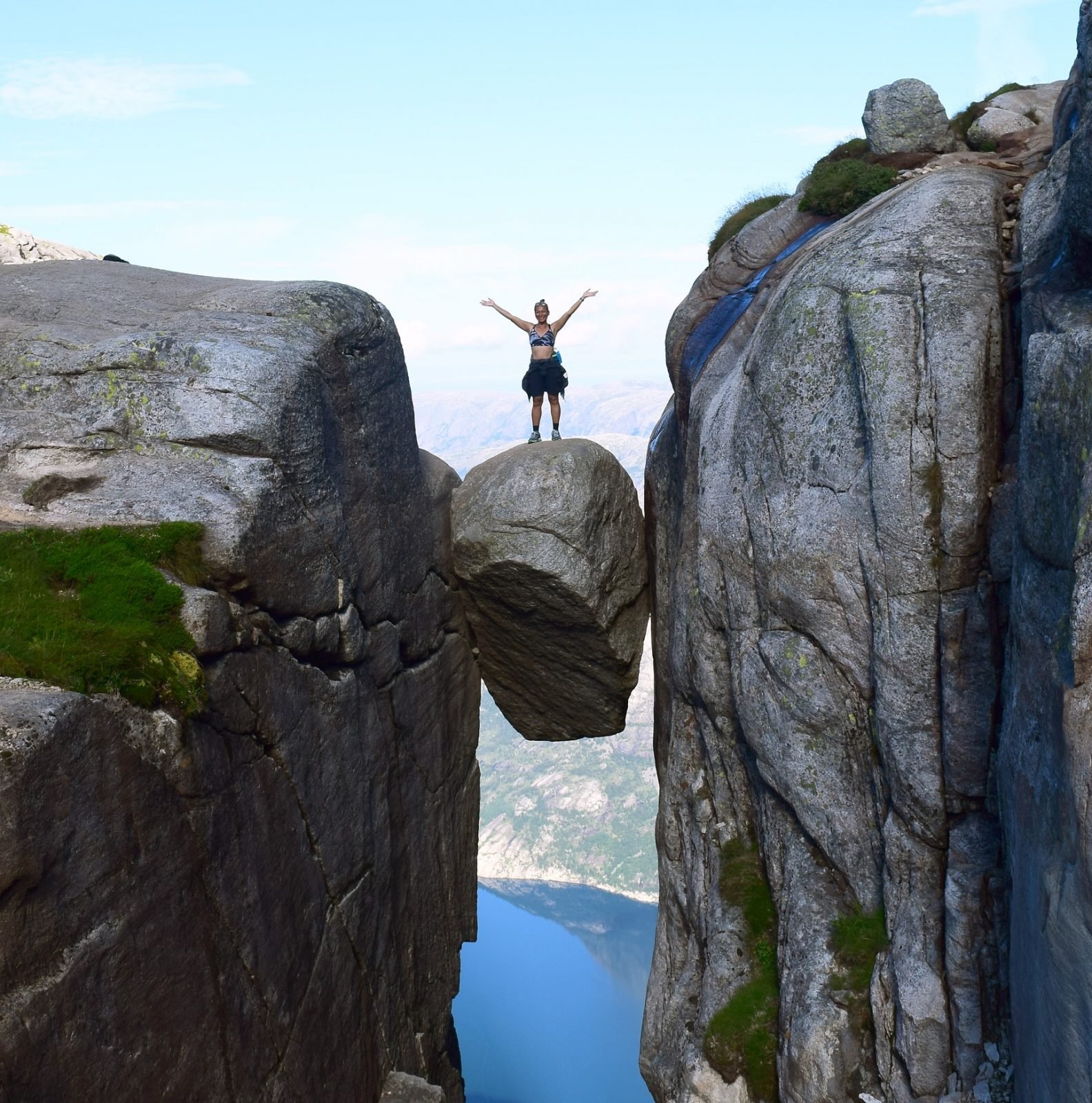 A tourist poses for a photo on a boulder jammed between two mountains in Kjeragbolten, Norway