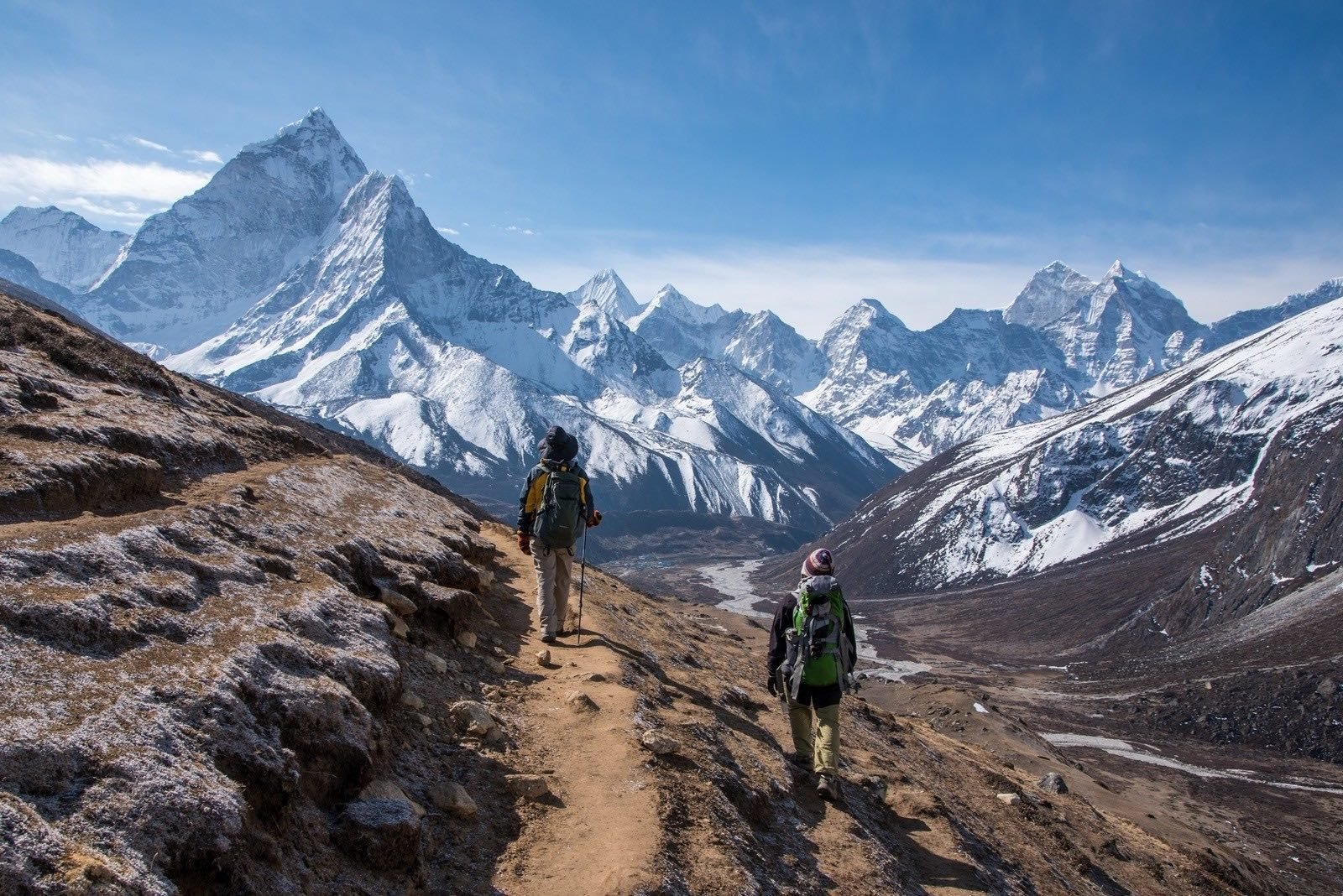 Two hikers trekking through the mighty mountains of the Himalayas, with a stunning mountainous backdrop.