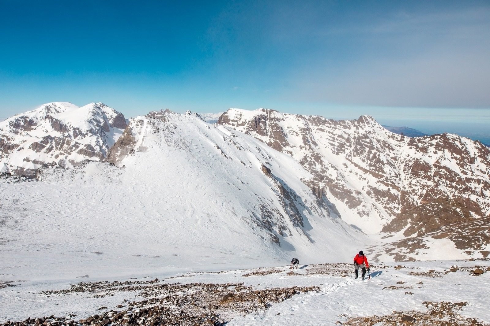 Two climbers make their way up a snowy, slippery hill at high altitude.