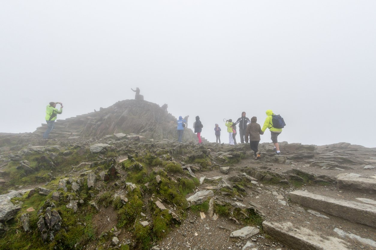 A small group of hikers in the fog at the very summit of Mount Snowdon in Wales