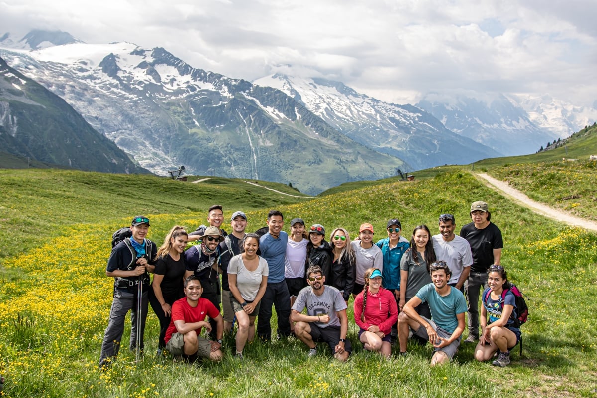 A tour group pose in an alpine meadow, with mountains behind.
