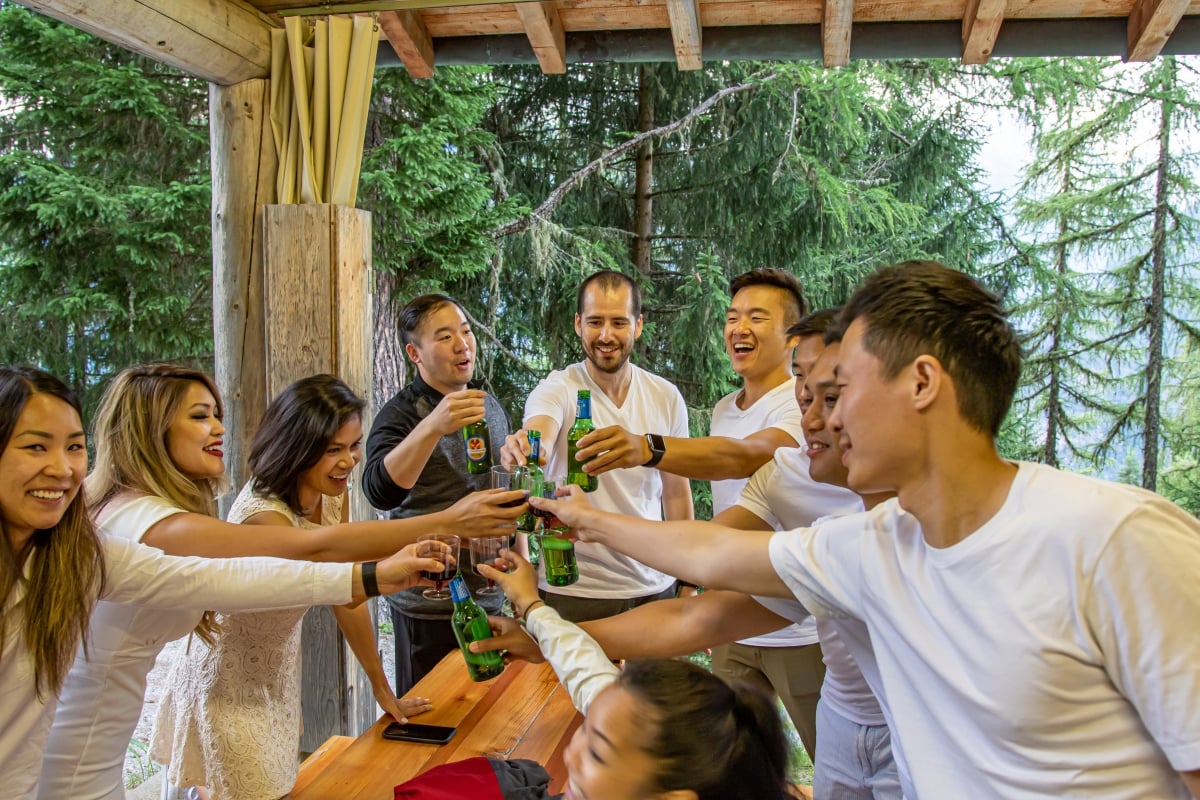 A group toast each other in a mountain hut, surrounded by forest.