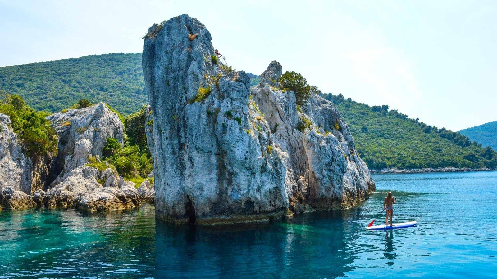 A woman on an SUP in Croatia, passing a rock.