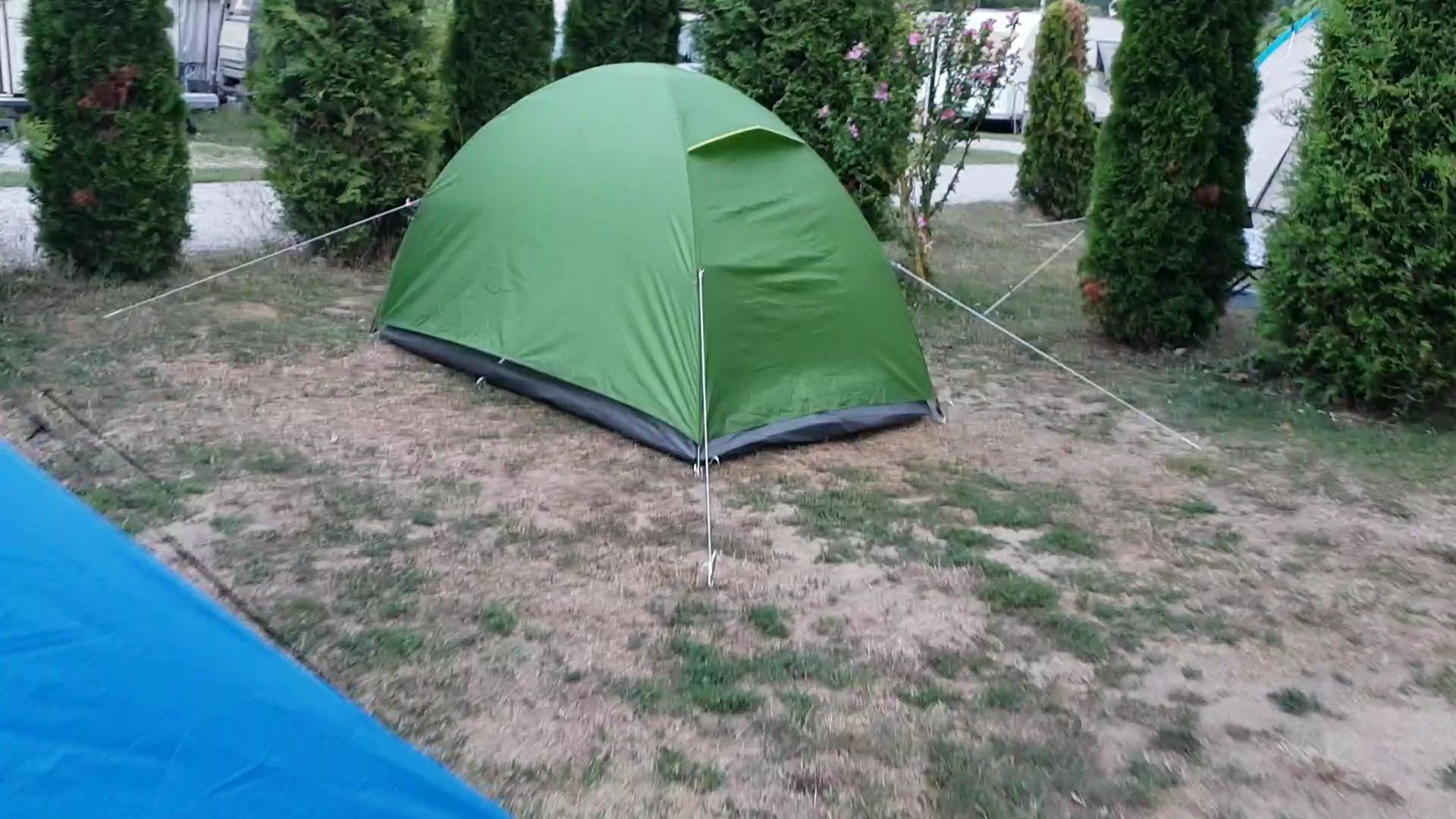 A small tent erected in the corner of a campsite.