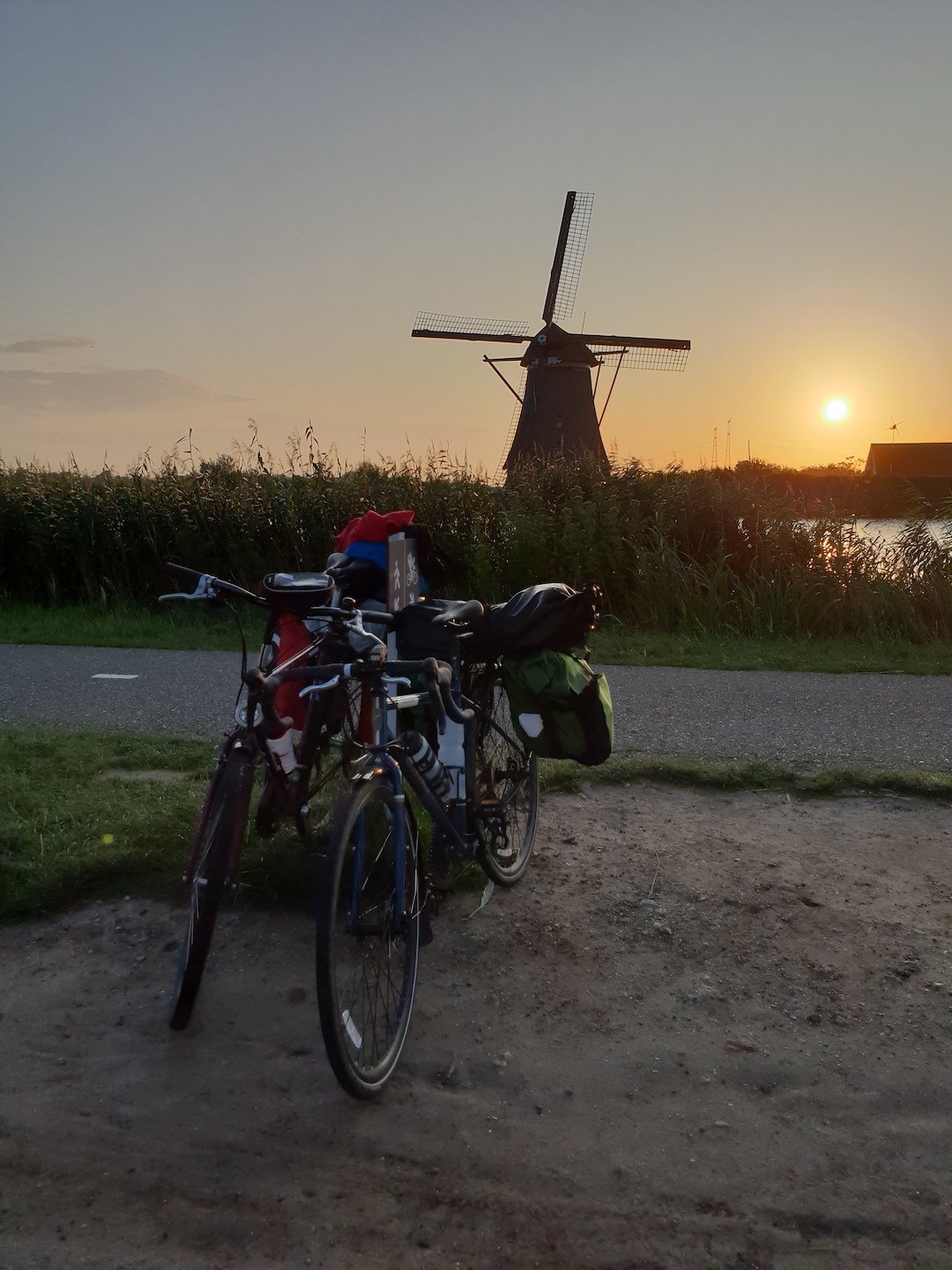 Two bikes, and a windmill at sunset behind.