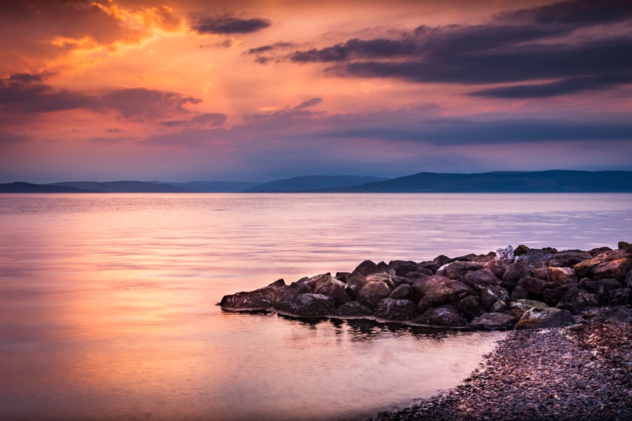 View of Wemyss Bay rocky sea coastline in Scotland, UK on a day with blue orange cloudy sky.