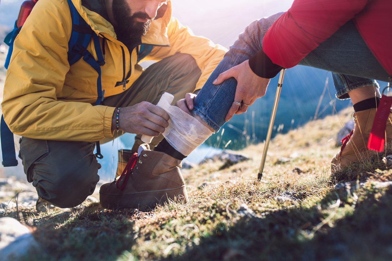 A male hiker wrapping a bandage around the cut leg of a woman hiker.