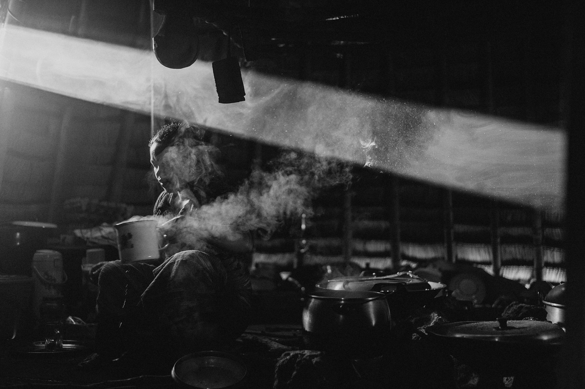 A woman drinking a pot of coffee inside a hut in Wae Rebo, Indonesia.